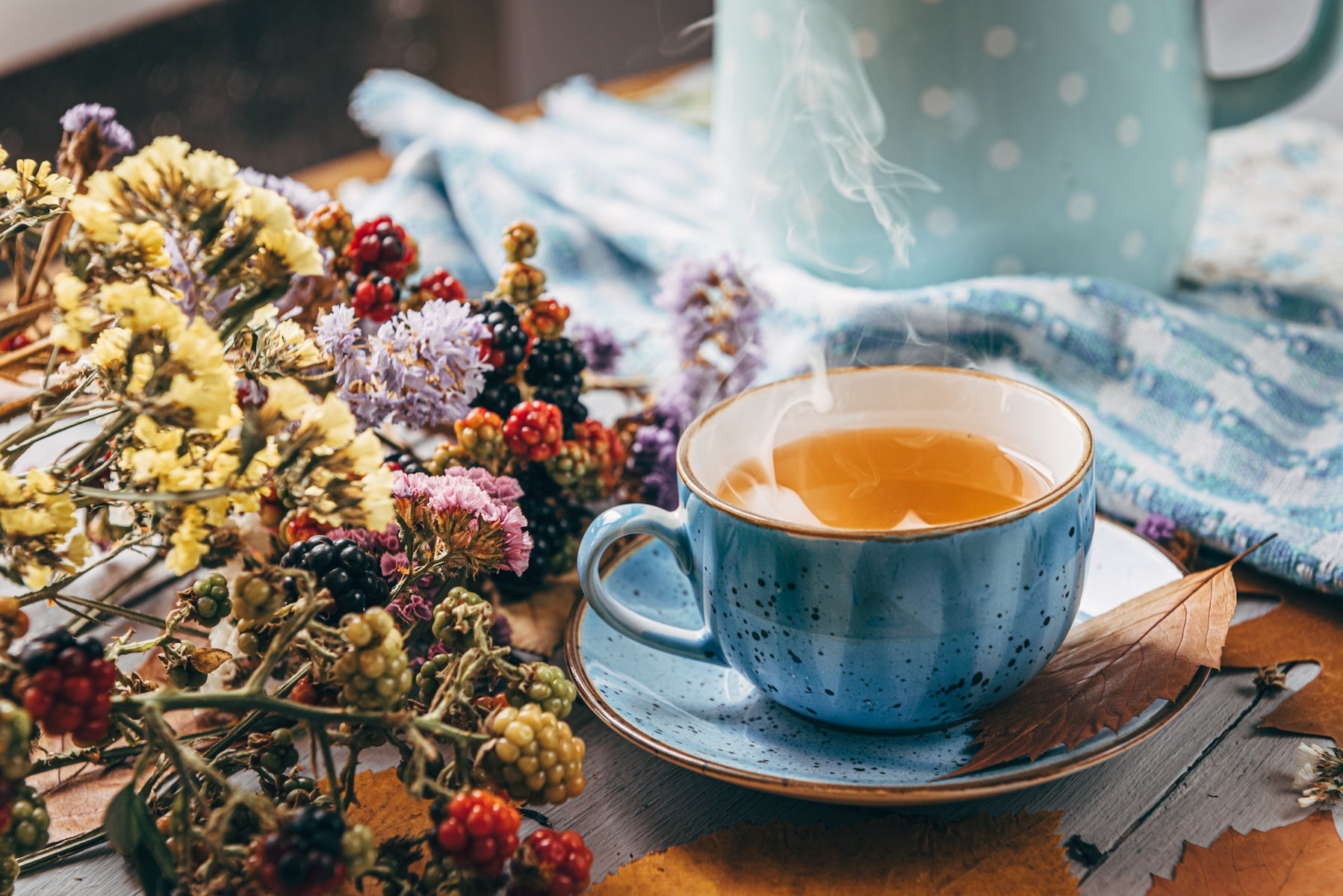 Steaming cup of tea surrounded by vibrant dried flowers and fresh berries.