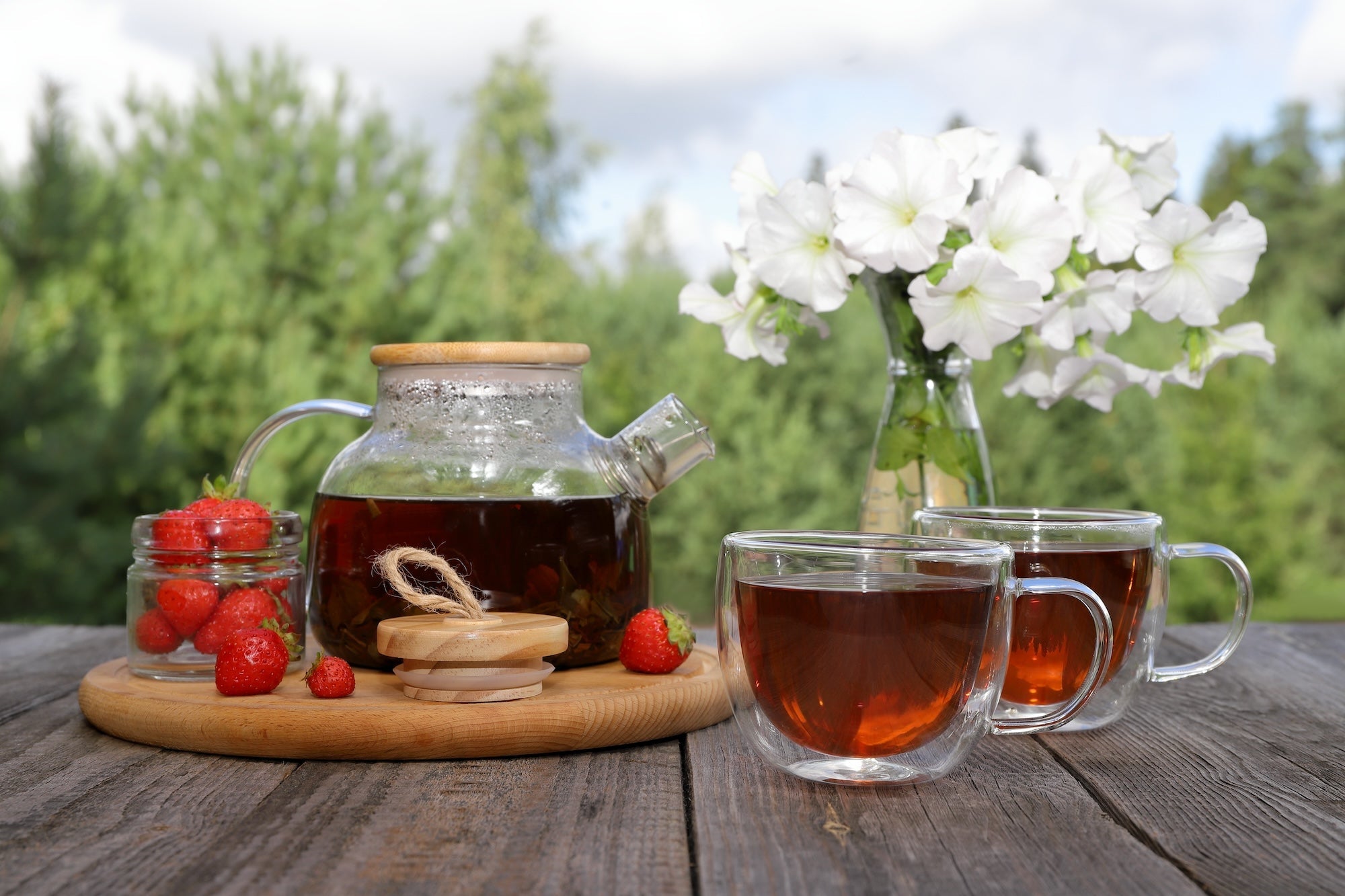 A refreshing pot of tea with fresh strawberries on a wooden table outdoors.